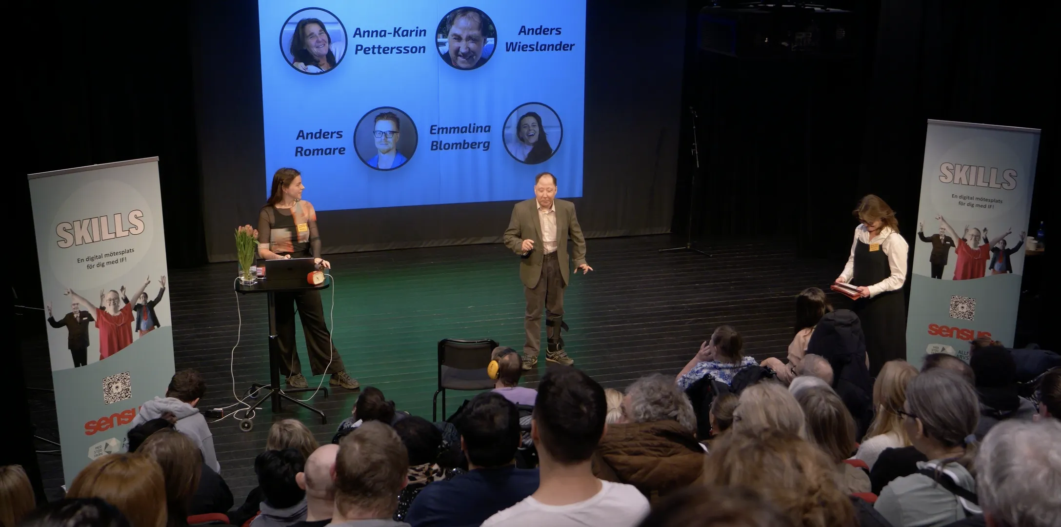 Presentatörer på en scen framför en publik under ett SKILLS-event. På den blå projektionsskärmen visas profilbilder av fyra talare. Roll-ups med SKILLS-logotypen står på vardera sida av scenen.